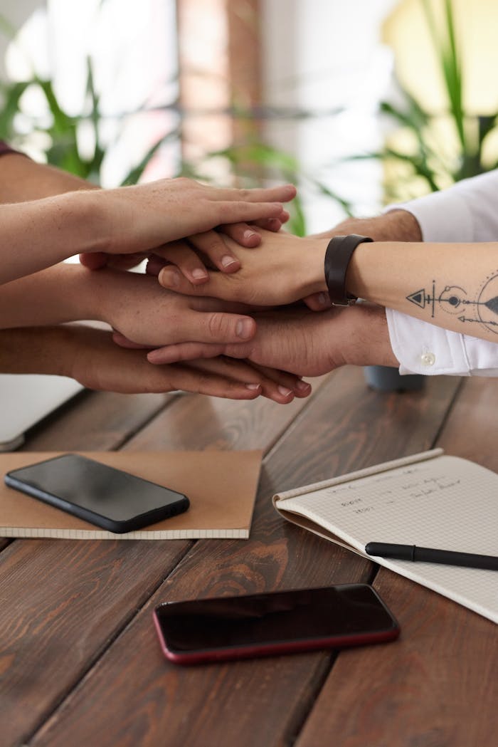 contact Hands from a diverse team stack on a table symbolizing unity and teamwork in a modern office setting.